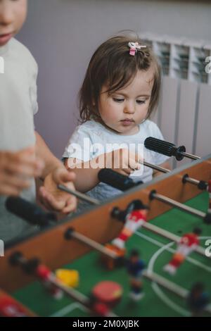 Baby girl having fun playing table football in a children's play entertainment center with her brother. Hobby and leisure Stock Photo
