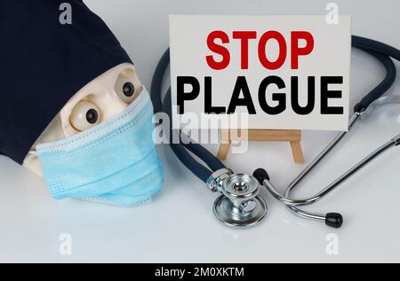 Medicine and health concept. Skull in mask and cap, stethoscope and easel with canvas on which it is written - STOP PLAGUE Stock Photo