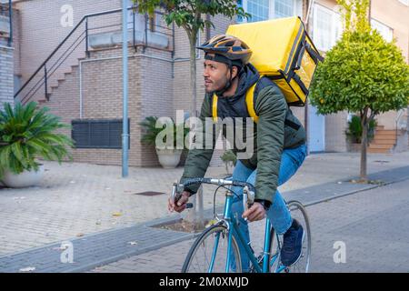 Young African American delivery man riding on bike. Black courier delivering food and drink in town. Stock Photo