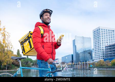 Food delivery concept. Smiling African American driver with backpack looking smartphone in the city Stock Photo
