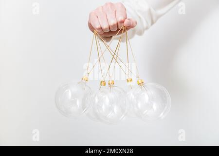 Female hand holding transparent glass Christmas balls on white backdrop. Trendy Christmas background Stock Photo