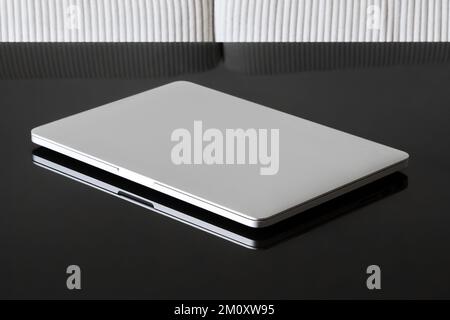 Laptop Closed. Laptop on a black glass table against a white sofa. Stock Photo