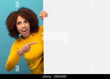 Discount black friday or sale african american woman peeking out from empty white board and pointing her finger Stock Photo