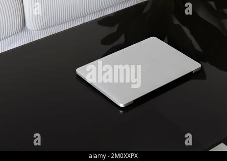 Laptop Closed. Laptop on a black glass table against a white sofa. Stock Photo