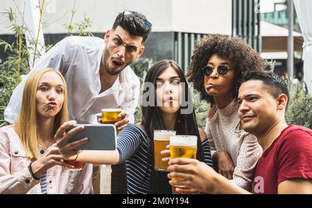 crazy selfie time of a millennials group of friends, people drinking beers and having fun using smartphone for making memories Stock Photo