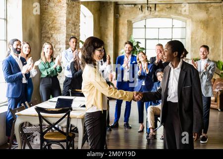 handshake between two business women to agree on the transition of deliveries, generations of entrepreneurs in comparison, large working group of the Stock Photo