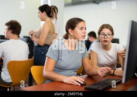 Schoolgirl using computer and teacher helping to him in class room Stock Photo
