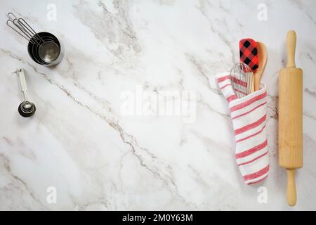 Rolling pin, tea towel, spatula,wooden spoon,whisk, measuring cups and spoons on marble background in flat lay format. with room for text. Stock Photo