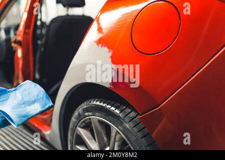 Mechanic's garage. Process of car damage repair. Red car covered with automotive filler and being prepared for varnishing. High quality photo Stock Photo
