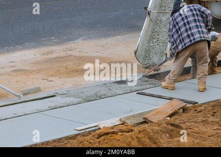 Workers are pouring cement on side of house in order to create new sidewalk Stock Photo