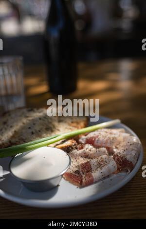 Close up view slices of smoked bacon meat with rye whole grain black bread, green onion and sour cream on the table. Stock Photo