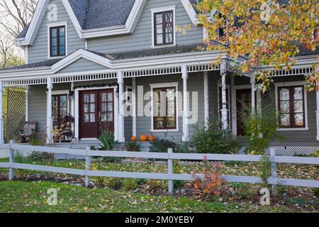 Grey clapboard and white trim two story Victorian country style home with landscaped front yard in autumn. Stock Photo