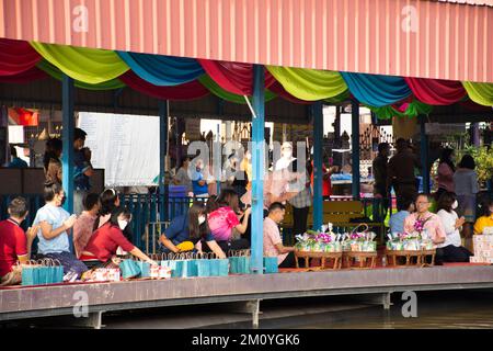 Thai people foreign traveler travel visit and join tradition merit ritual and praying offering alms giving to monk procession on boat in canal at Wat Stock Photo