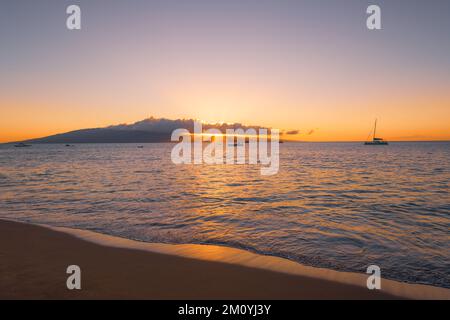 Tropical sunset over an island, sailboats, ocean, and sandy beach at Kaanapali Beach in Maui, Hawaii Stock Photo
