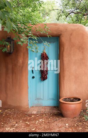 Turquoise door with red chile ristra in adobe wall in Santa Fe, New Mexico Stock Photo