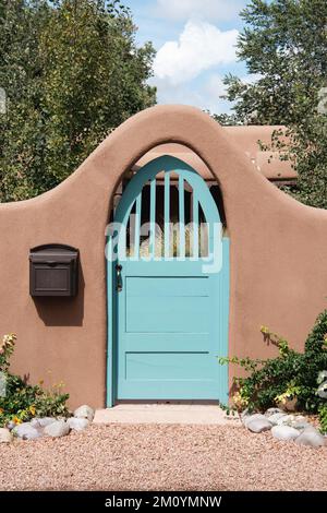 Turquoise gate in an arched entrance to a garden through an adobe wall in Santa Fe, New Mexico Stock Photo