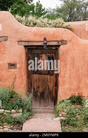 Weathered wood door and old adobe wall with flower pots with red flowers in Santa Fe, New Mexico Stock Photo
