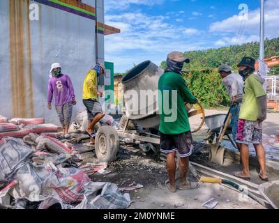 Puerto Galera, Philippines - April 9, 2022: A crew of Filipino workers using a portable concrete mixer on a construction site on Mindoro Island. Stock Photo