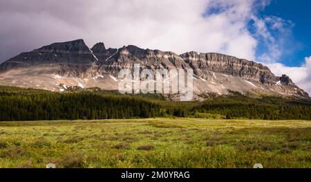 Panorama of a rugged mountain range and grassy meadow under a dramatic sky in Glacier National Park, Montana Stock Photo