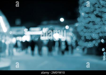 Blurred background. Christmas tree, decorated glowing lights, building silhouettes of people walking city square at winter night. Beautiful New Year and Christmas holiday blurred background Blue color Stock Photo