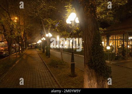 Light poles arranged in a row in the evening. Street lanterns glow with bright warm light. Stock Photo