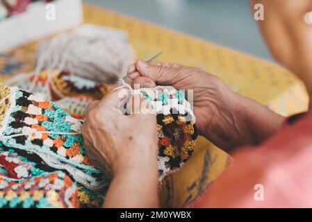 Close up of old female hands doing knit work with wool at home for indoor leisure activity. Aged retired female people knitting work alone at home. El Stock Photo