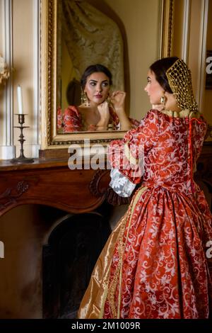 Beautiful woman in renaissance gown looking into an antique golden mirror in her castle Stock Photo