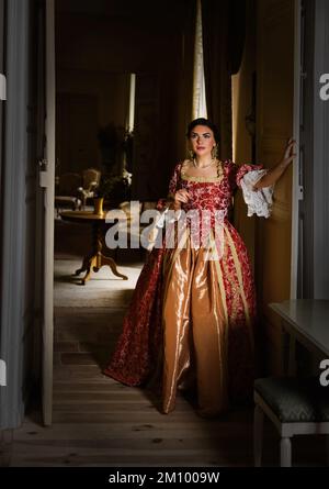 Beautiful woman in late renaissance costume posing between the open doors of a medieval castle. Stock Photo