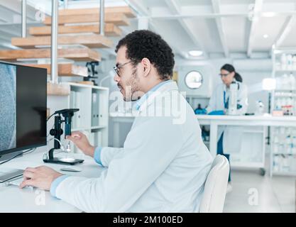 Science is such a vital channel of knowledge. a young scientist using a digital microscope while working on a computer in a lab. Stock Photo