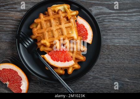 Waffles and grapefruit in a black plate on a wooden table Stock Photo