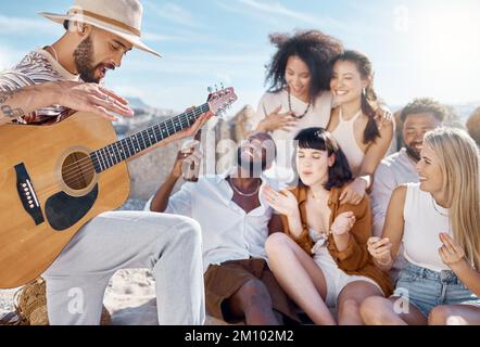 My friends are my biggest supporters. a man playing the guitar while his friends sing along at the beach. Stock Photo