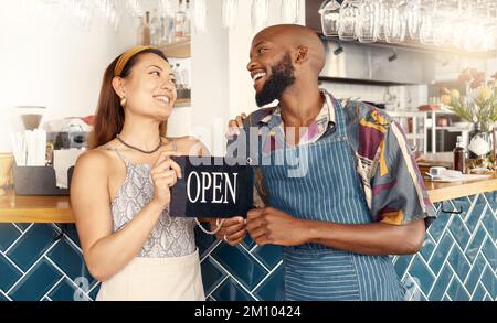 Pursuing their dreams together. two business colleagues working together holding an open sign. Stock Photo