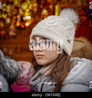 Portrait of thoughtful young woman wearing warm white hat with eyeglasses on city street and looking at camera. Beautiful student with cap and winter Stock Photo