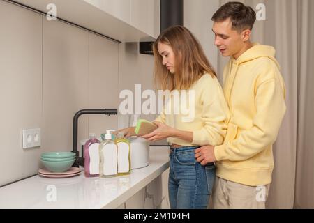 Cheerful happy man and woman washing the dishes using dishwashing liquid with blank label Stock Photo