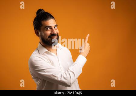 A handsome Hispanic male pointing his finger to an orange wall with copy space Stock Photo