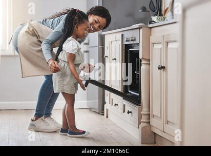 These are going to be delicious. a little girl and her mother standing in front of the oven. Stock Photo