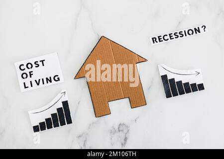 graphs with cost of living going up and economic growth going down due to recession next to cardboard house, concept of post pandemic economy during w Stock Photo