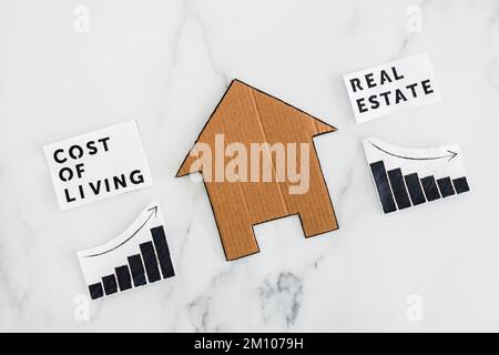 graphs with cost of living going up and real estate transaction going down next to cardboard house, concept of post pandemic economy during winter 202 Stock Photo