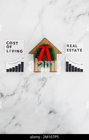 graphs with cost of living going up and real estate transaction going down next to cardboard house with Christmas wreath, concept of post pandemic eco Stock Photo