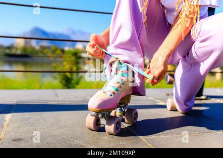 close up photo of legs woman in bell-bottomed trousers with pink pastel color roller skates outdoors in sunny day Stock Photo