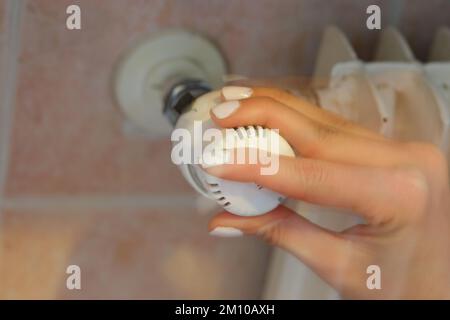 Hand regulating the white Thermostatic Valve for setting the temperature of the radiators for energy saving Stock Photo