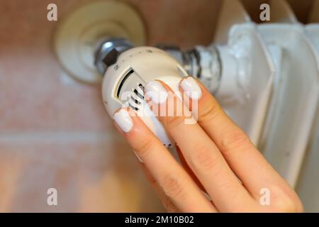 Hand regulating the white Thermostatic Valve for setting the temperature of the radiators for energy saving Stock Photo