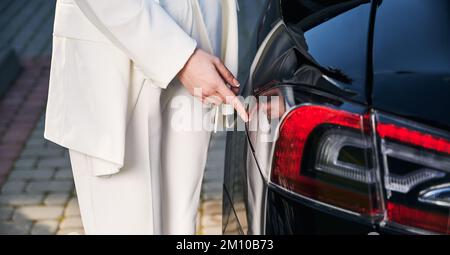 Close-up view of female one hand pointing to place on electric car for connect charger. Stock Photo