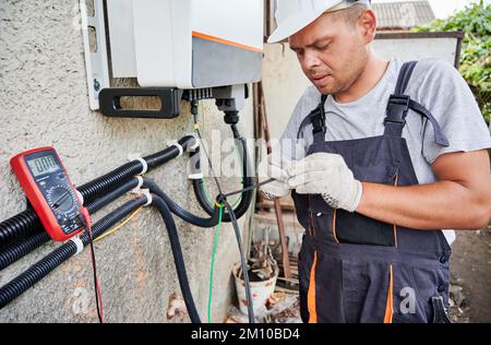 Man electrician installing solar panel system. Inspector in gloves making electrical wiring inverter and electric box. Concept of alternative and renewable energy. Stock Photo