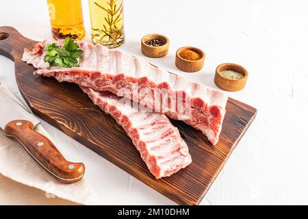 raw juicy pork ribs on a wooden cutting board with various spices in bowls for making a marinade. white background Stock Photo