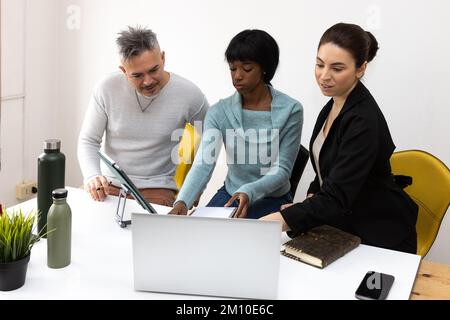 Multiethnic group of coworkers analyzing a project in the office. Desk with computer, smartphone, diaries and ecological water bottles Stock Photo
