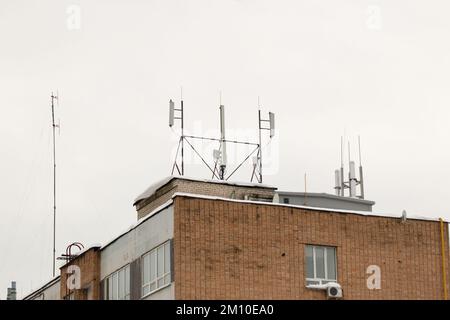 Many different cellular antennas on the roof of the house provide communication. Snow lies on the milestone, against the background of a gray sky. Cloudy, cold winter day, soft light. Stock Photo