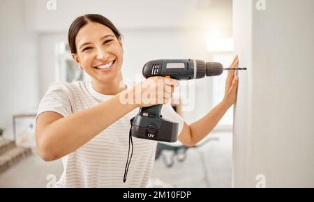 Im hanging a picture frame up here. an attractive young woman standing alone in her home and using a power drill. Stock Photo