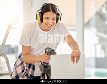 I like to spend my weekends doing woodwork. an attractive young woman standing alone in her home and using a power drill. Stock Photo