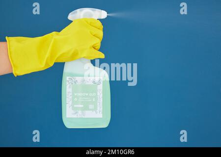 Hand, spray and detergent for cleaning, hygiene or anti bacteria chemical against a blue studio background. Hands of glove spraying liquid bottle for Stock Photo